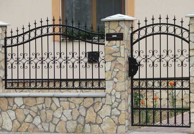 Decorative black metal fence and pedestrian gate between stone columns