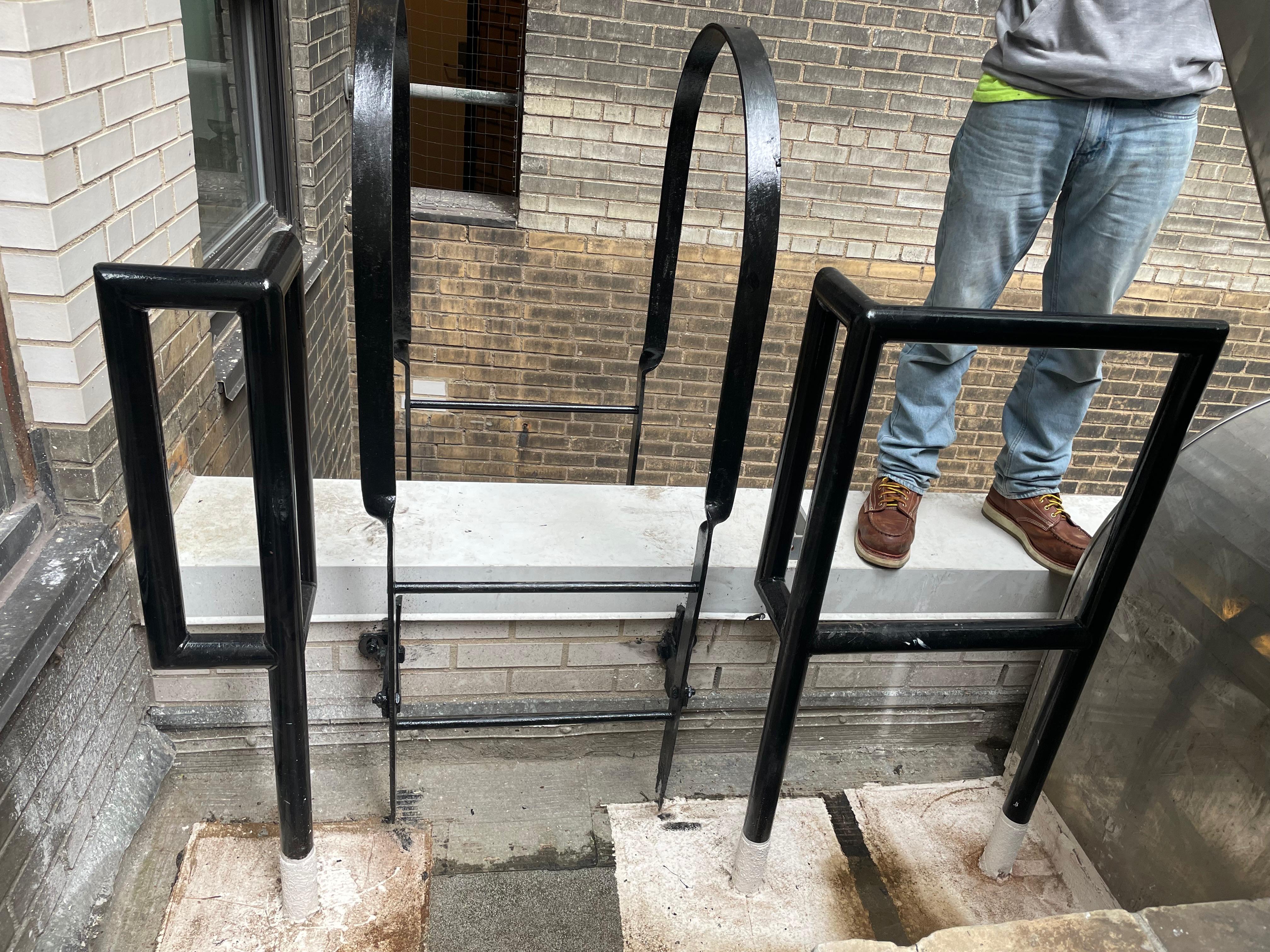 Black roof access ladder with curved extensions and adjacent metal handrails