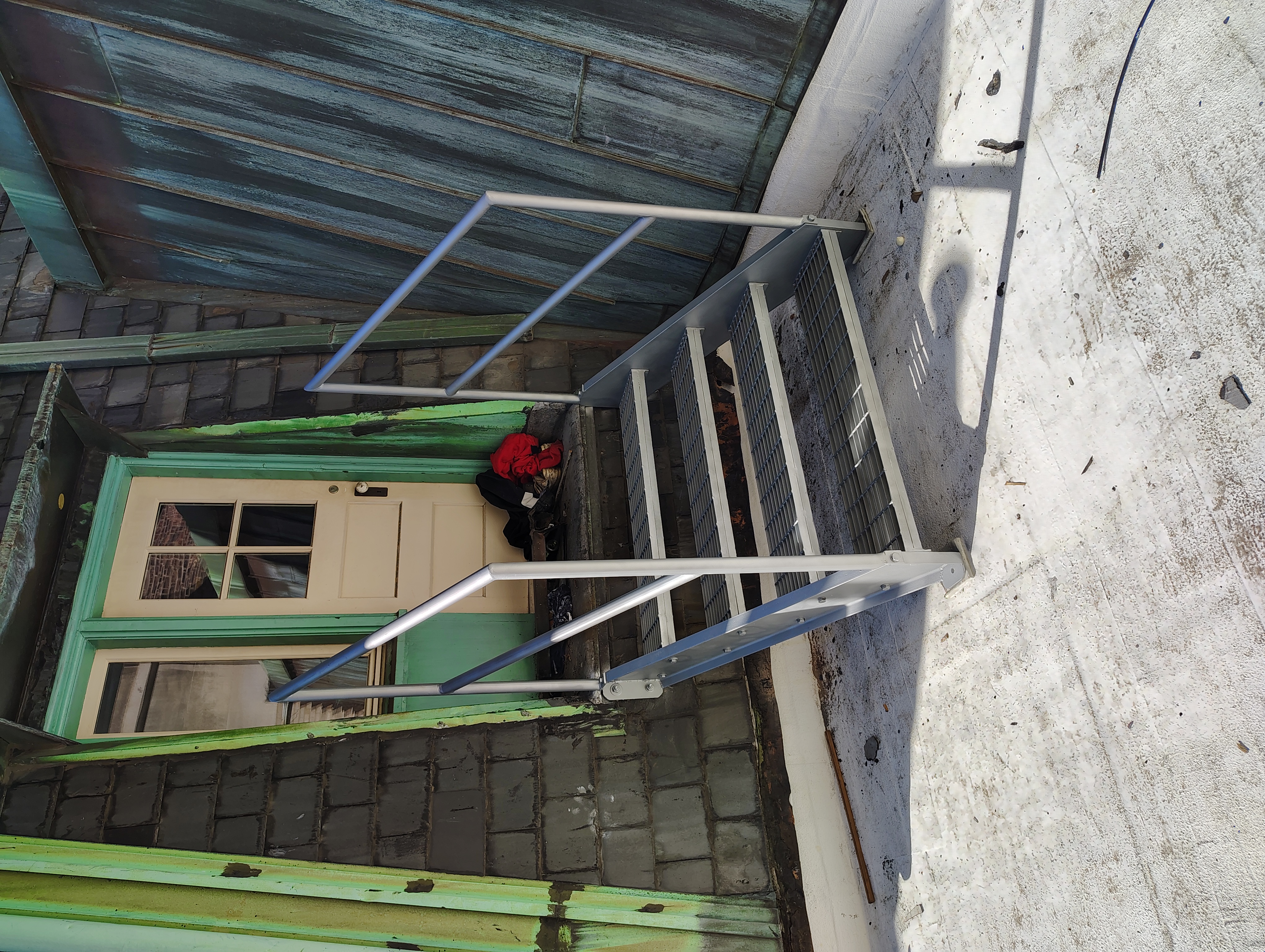Four steel grating steps with tubular handrails at a rooftop doorway