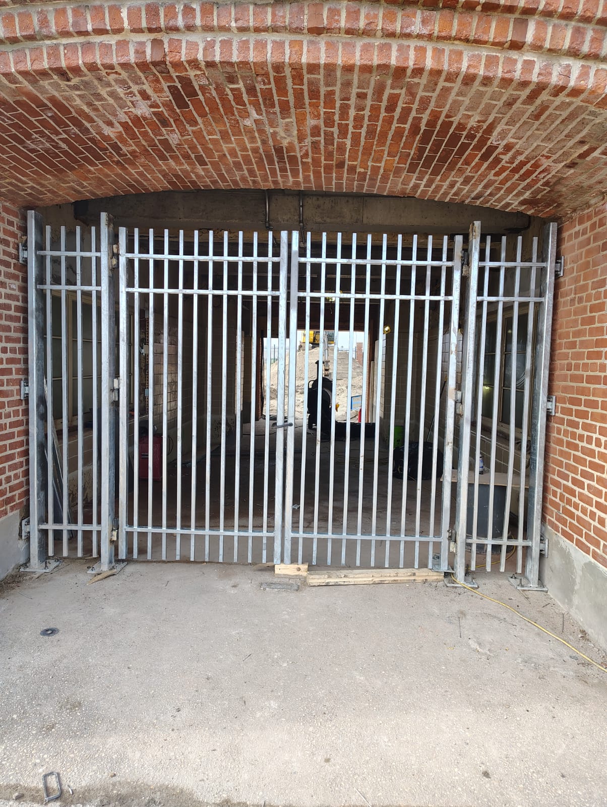 Double metal gate with vertical bars and fixed side panels under a brick arch