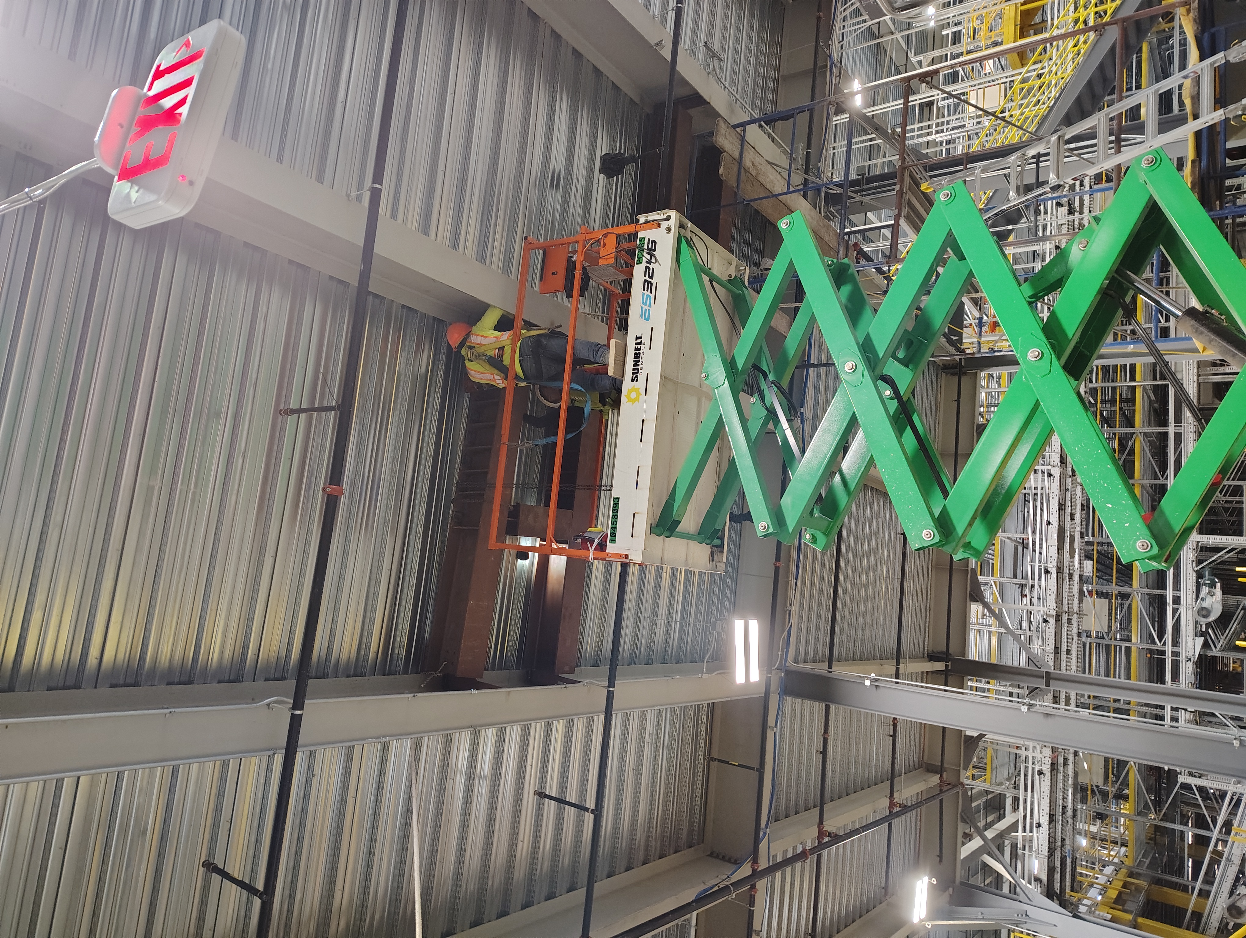 Worker on a scissor lift installing steel members beneath metal decking