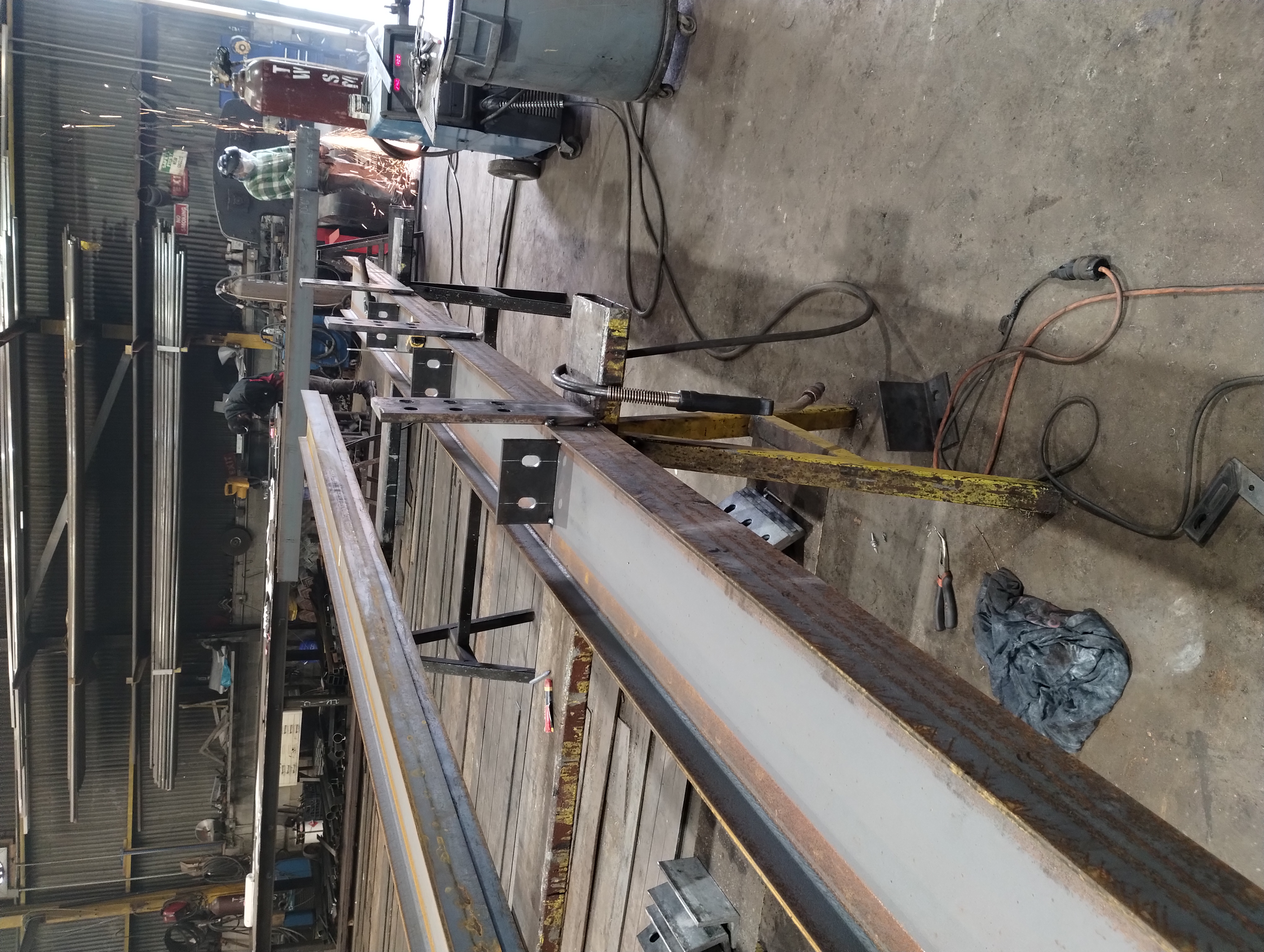 Steel beams on workshop tables with workers fabricating metal components