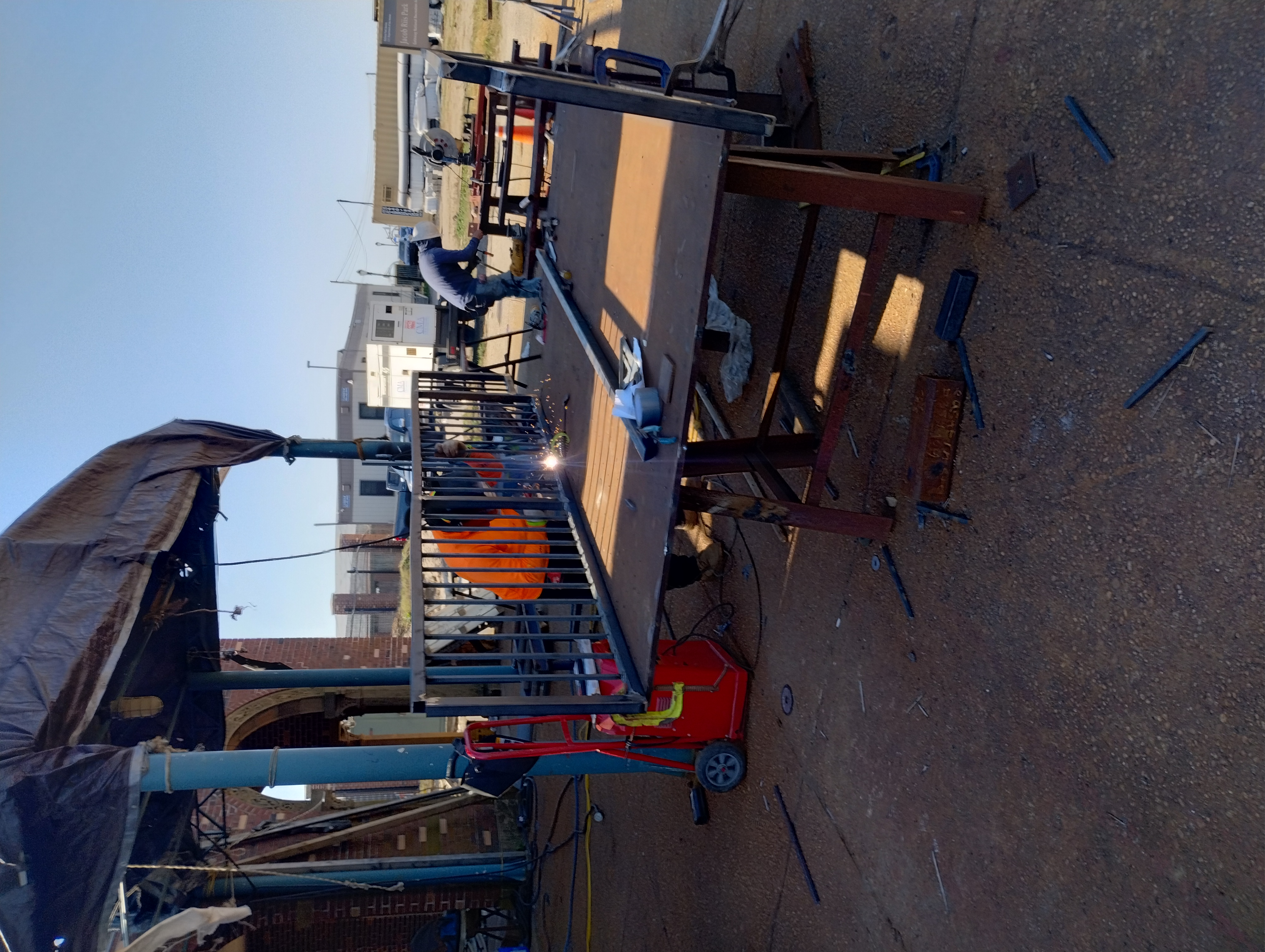 Welder joining a vertical-bar steel railing panel on an outdoor work table