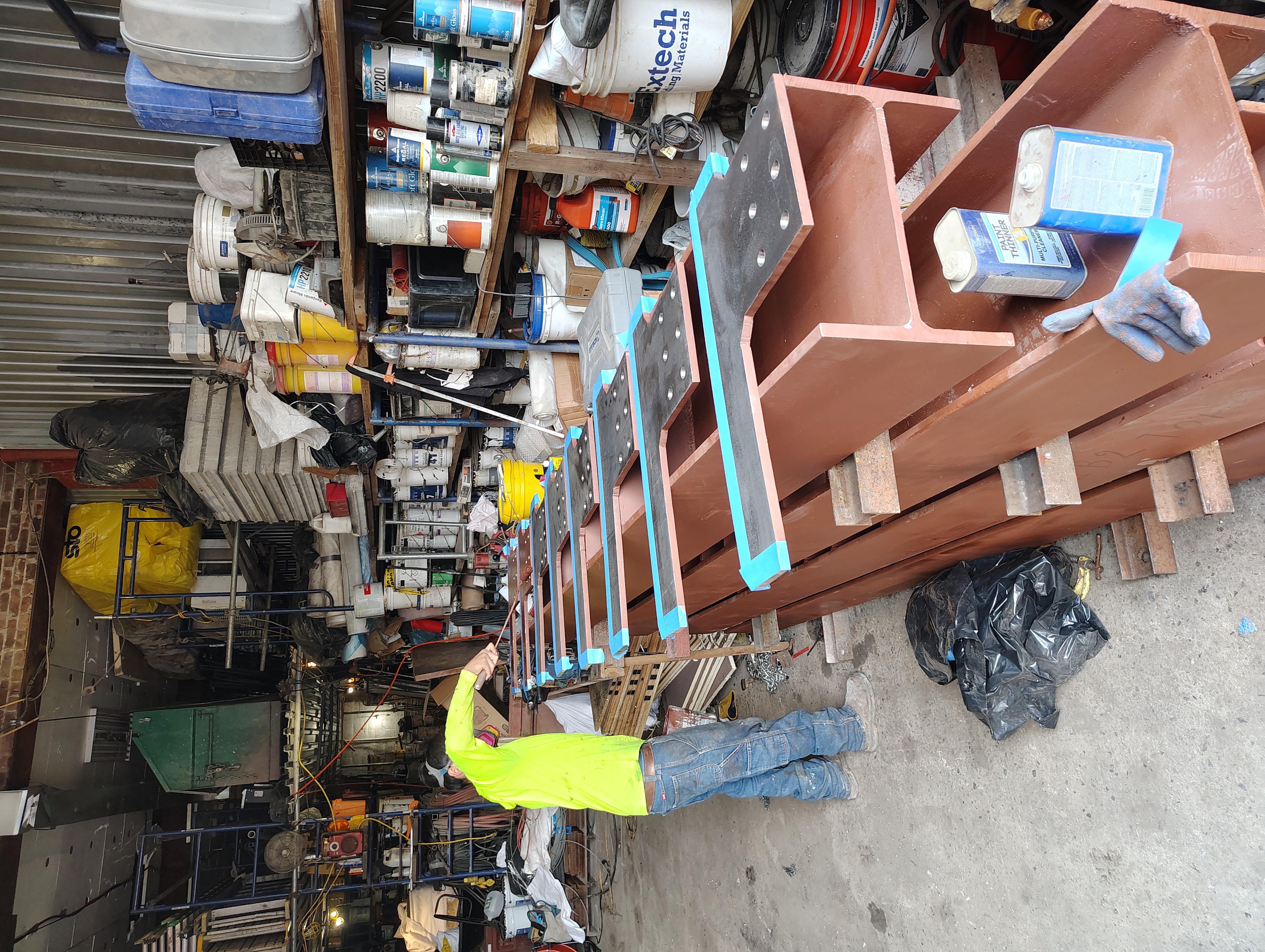 Worker applying coating to fabricated steel connection plates in a workshop