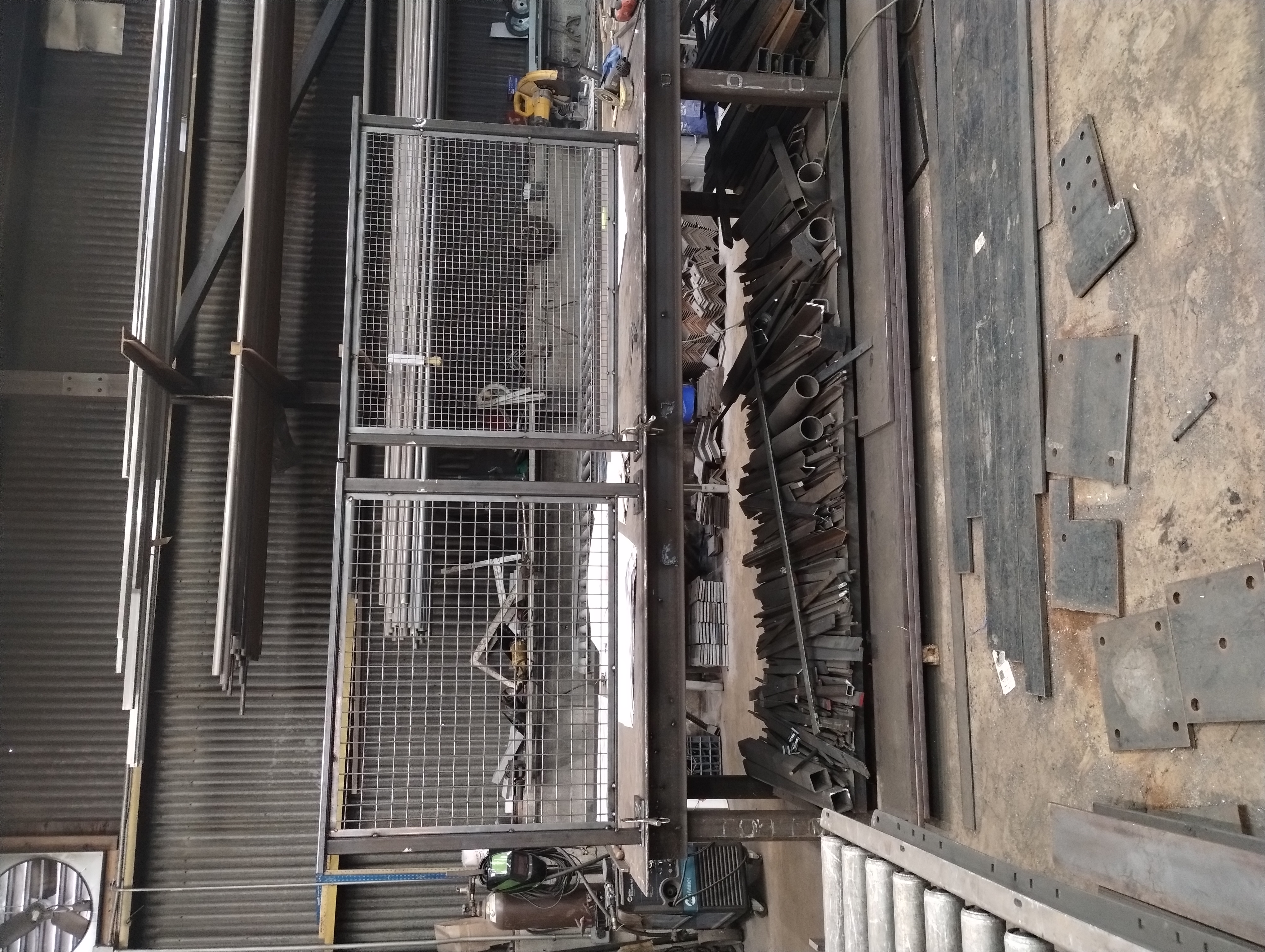Unfinished steel railing frames with wire mesh infill on a workshop table