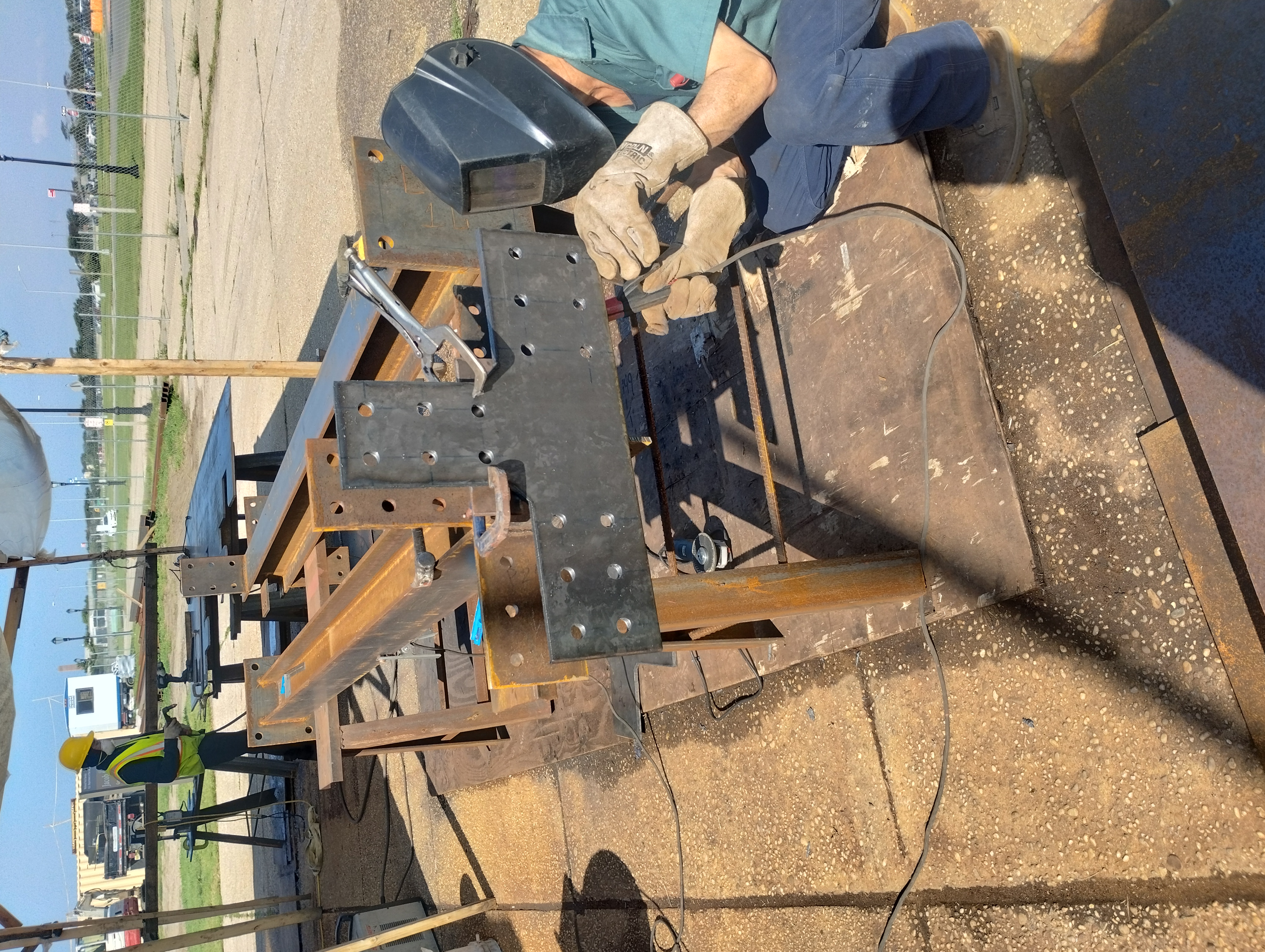 Welder working on steel connection plates in an outdoor fabrication area