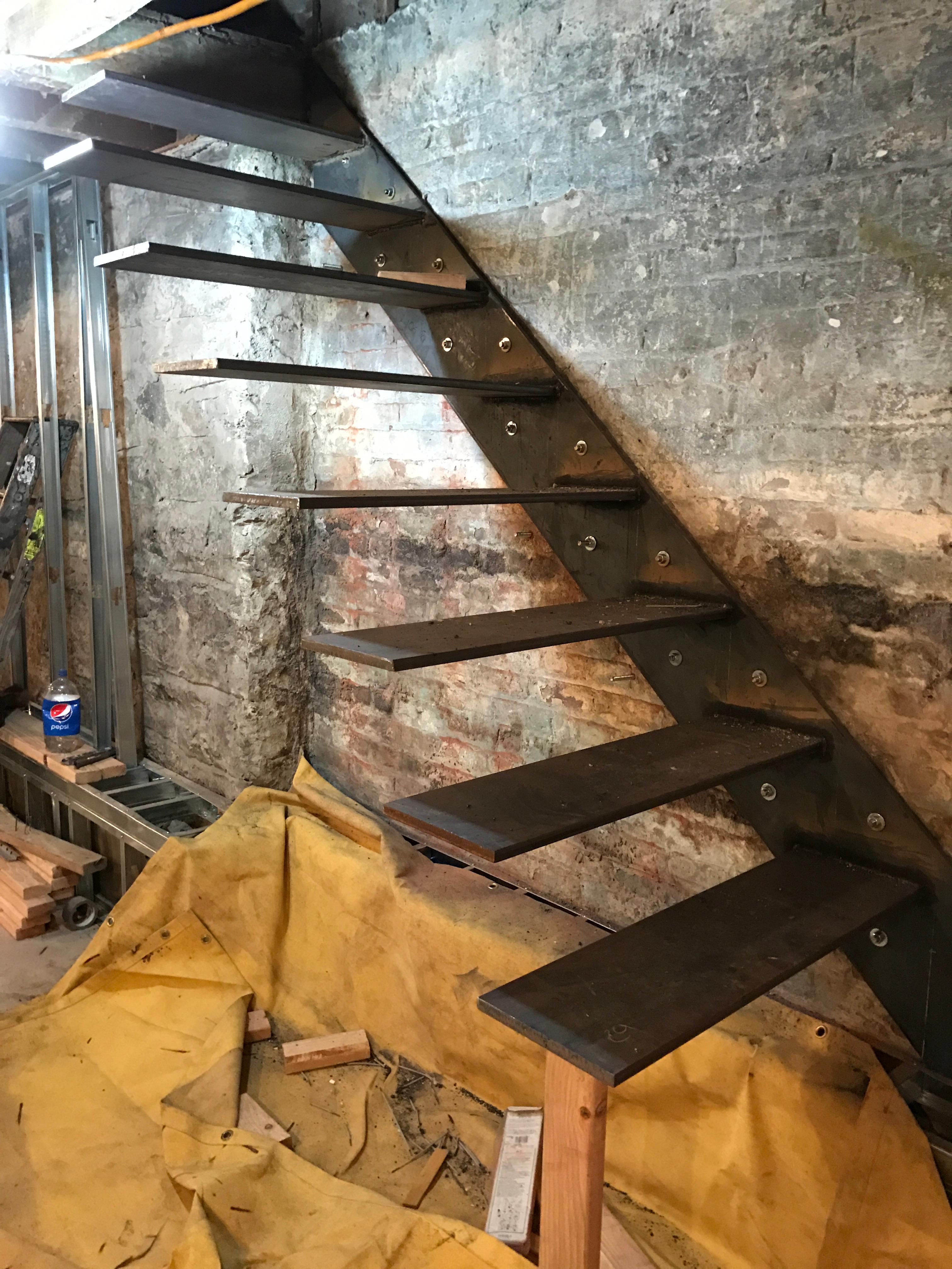 Cantilevered steel tread supports welded to a wall-mounted steel plate