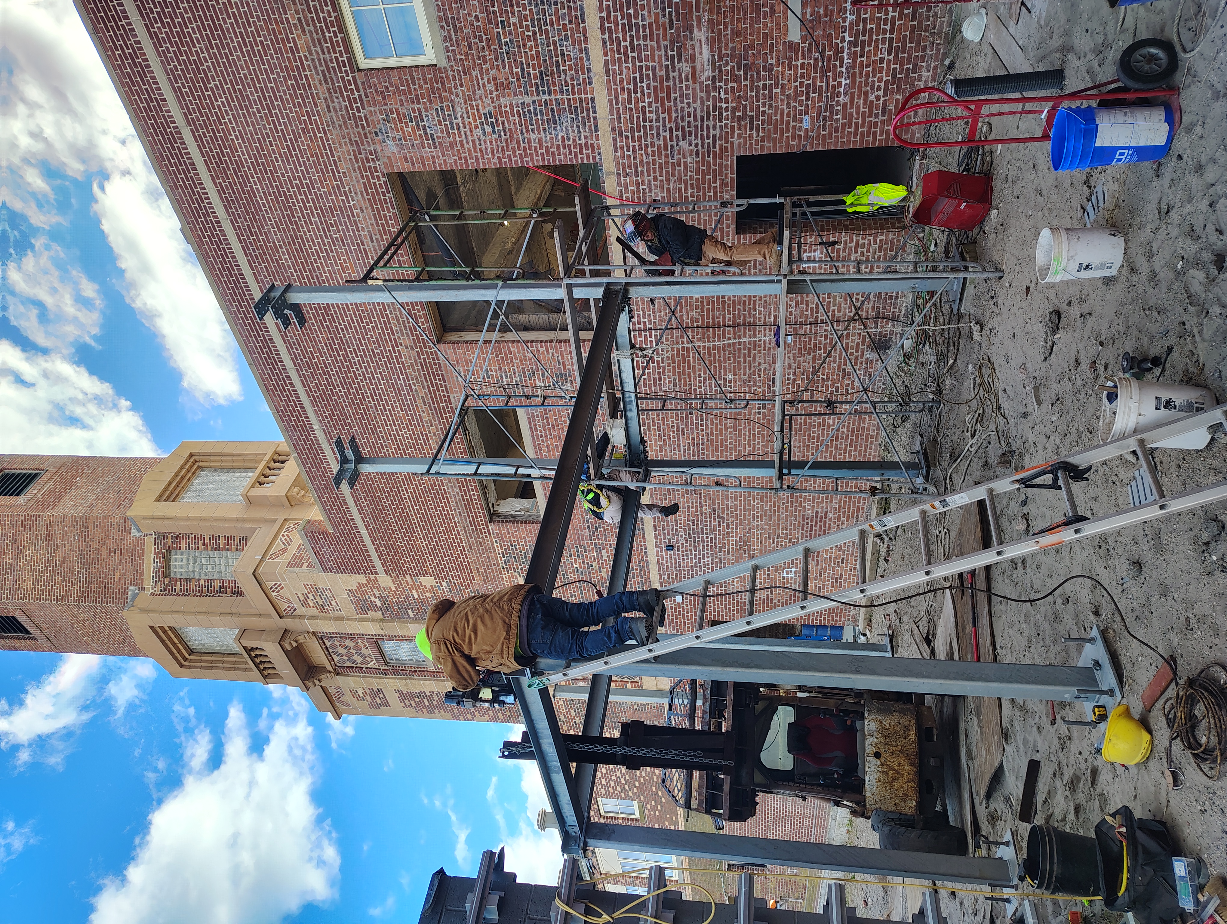 Crew installing steel beams and columns beside a brick building