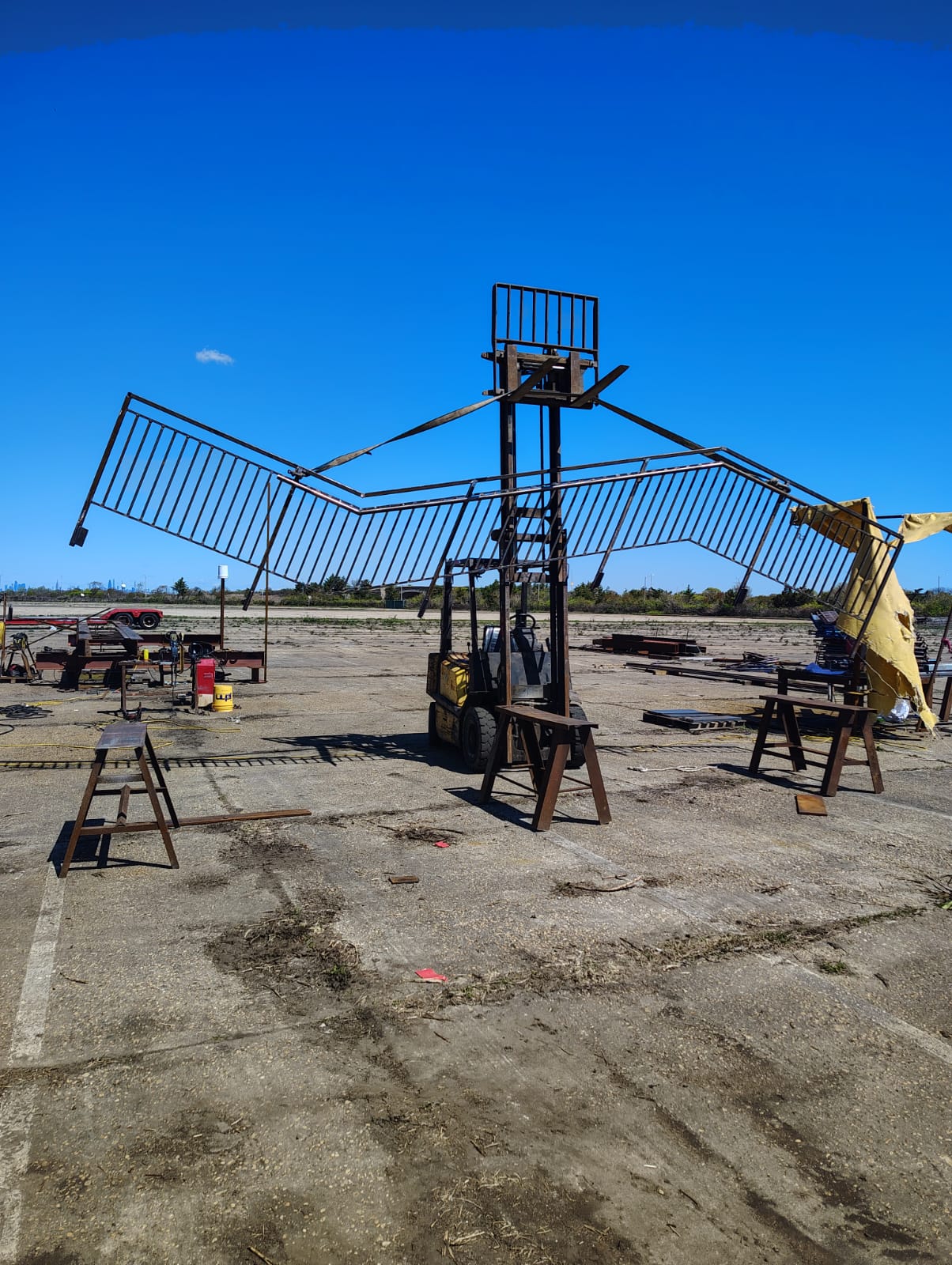 Long steel stair railing assembly suspended from lifting equipment in a fabrication yard