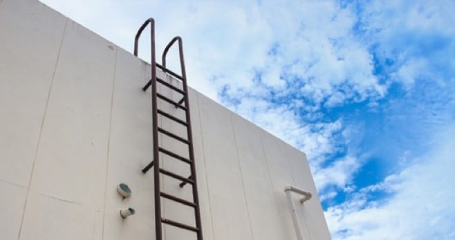 Wall-mounted steel ladder extending above a roof parapet