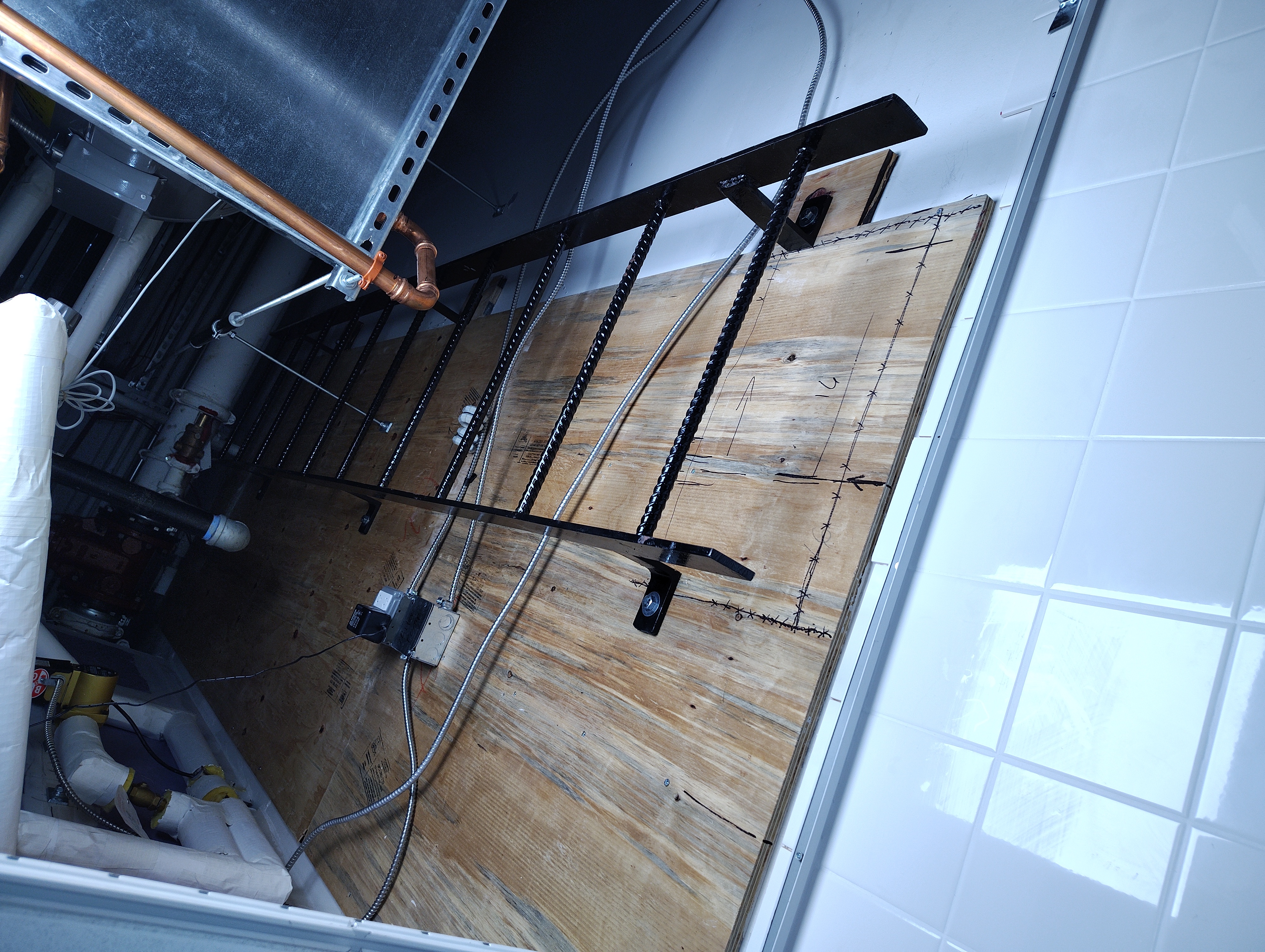 Wall-mounted black steel access ladder beside ducts and pipes