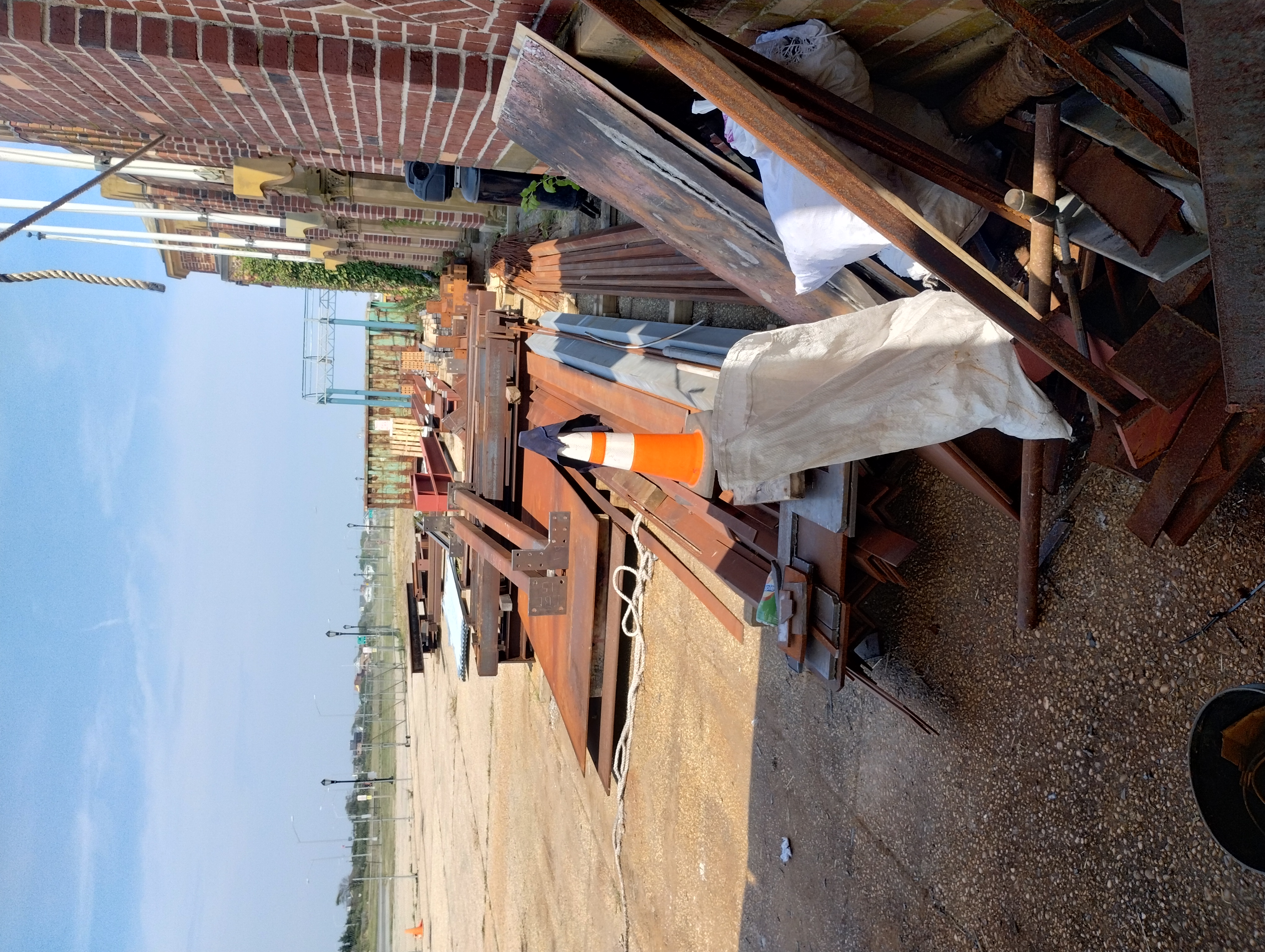 Steel beams, plates and fabricated components staged beside a masonry building