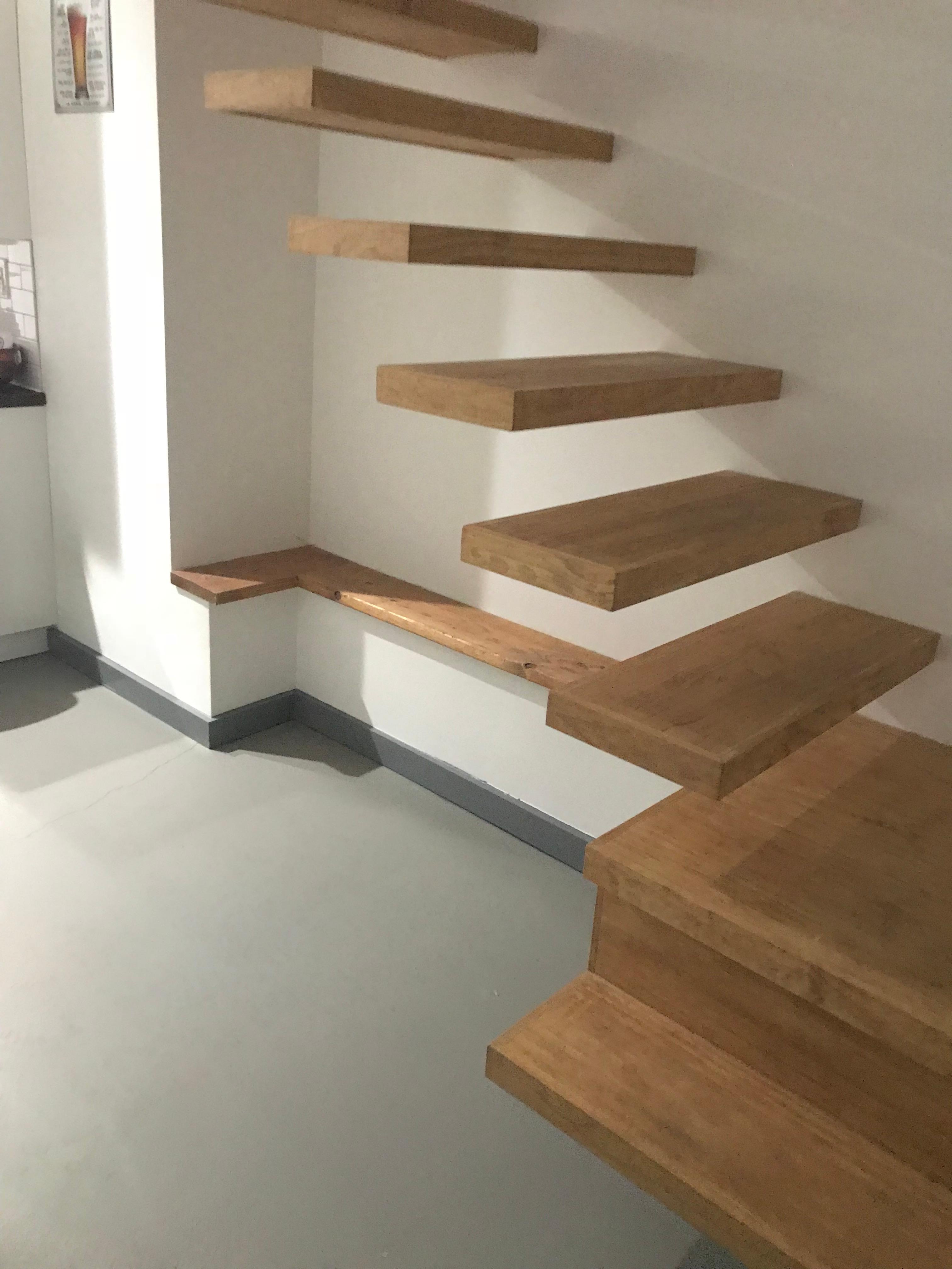 Floating staircase with thick timber treads beside a white wall