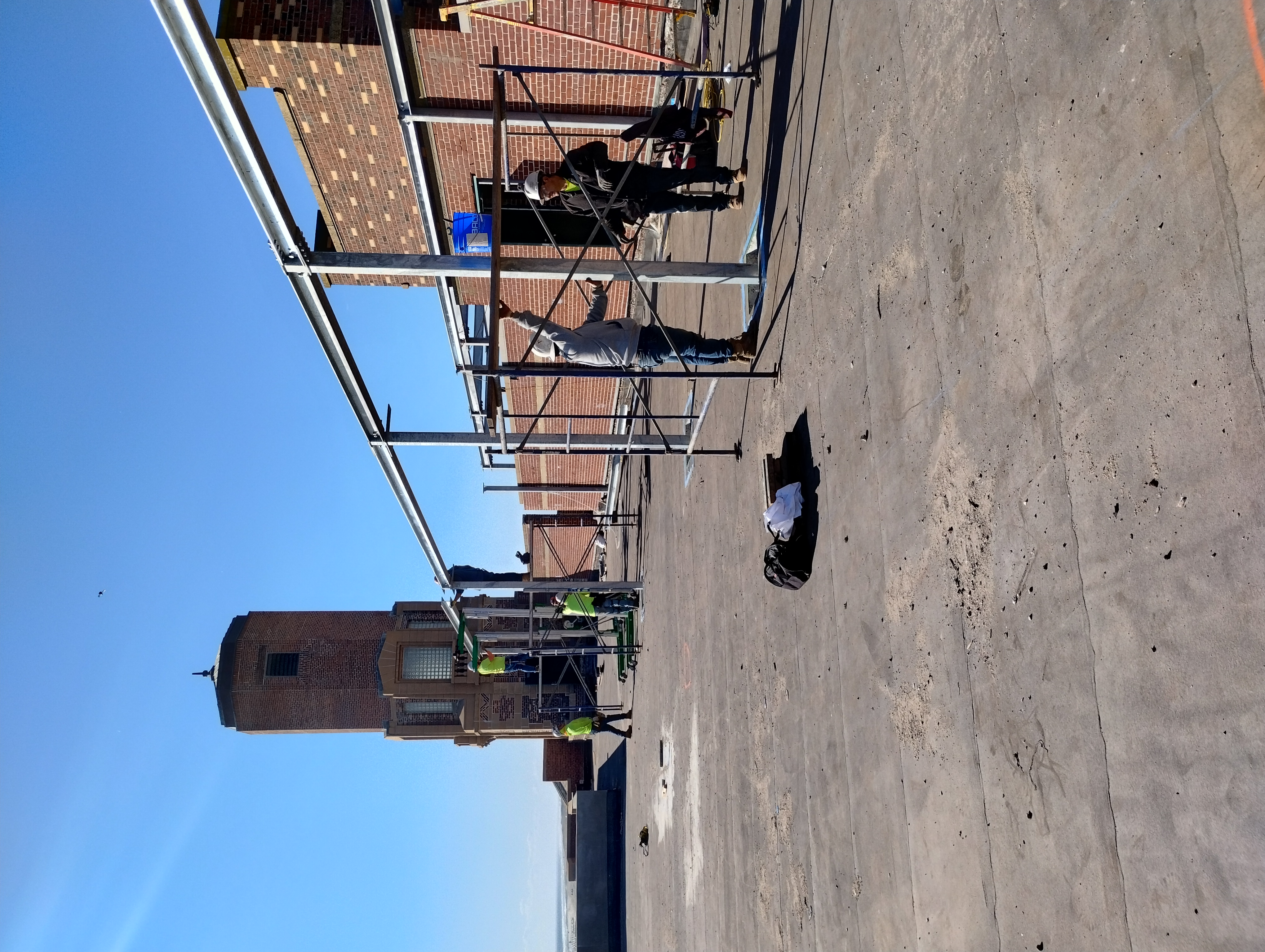 Crew erecting rooftop steel beams and columns alongside a brick wall